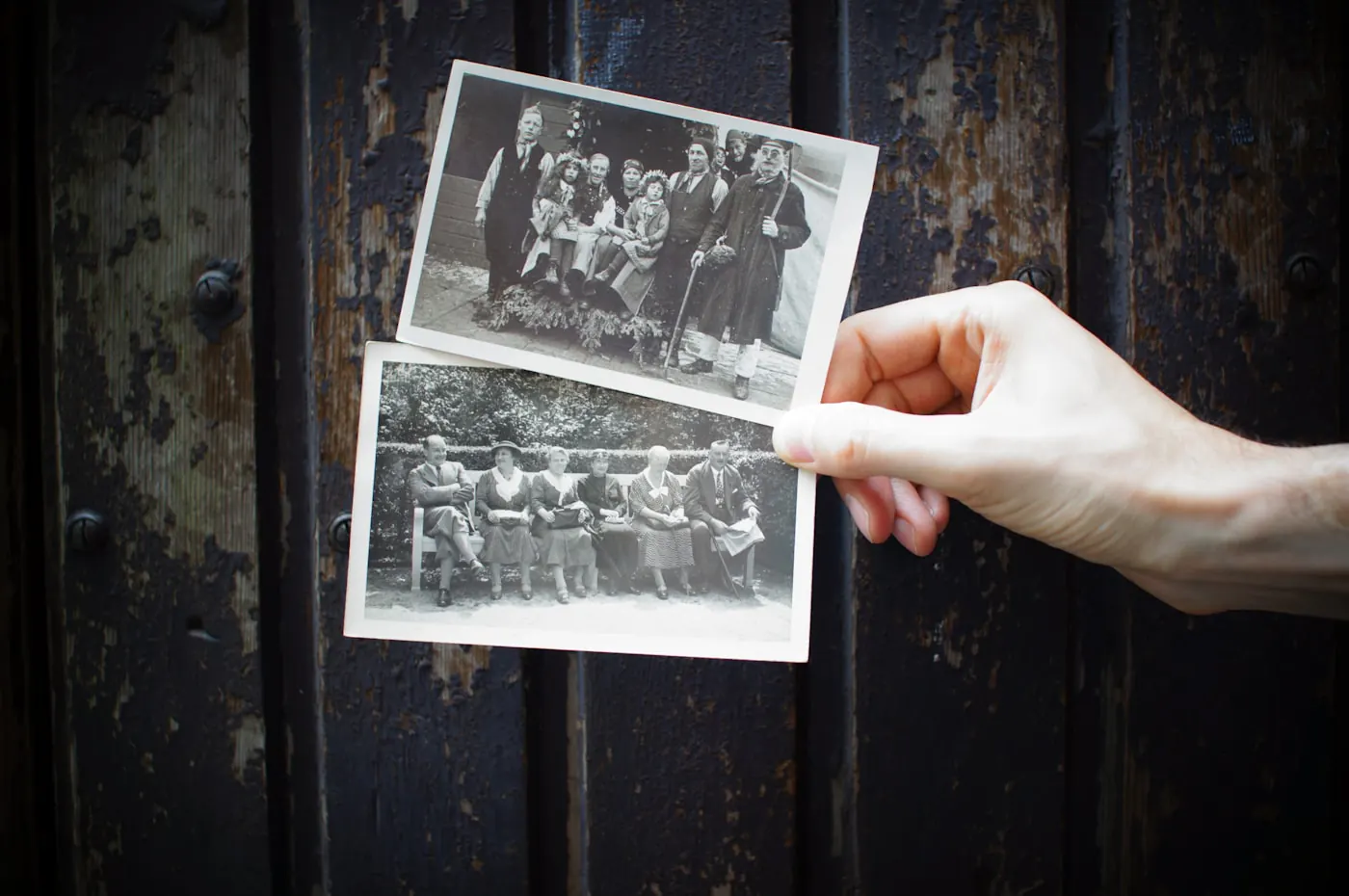 Une main tient deux photographies anciennes de famille devant une porte en bois.